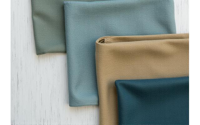 Ulike tekstilprøver i jordnære blå- og grønntoner, arrangert på en treoverflate. Fargene ser naturlige ut, som fra tang og alger.